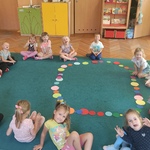 Dzieci z grupy II siedzą na dywanie i układają kolorowe koła origami.