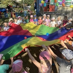 Dzieci trzymają chustę animacyjną, na której są małe kolorowe piłki.