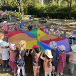 Dzieci trzymają chustę animacyjną, na której są małe kolorowe piłki.