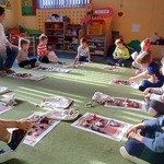 Dzieci siedzą w kole na dywanie z planszami podczas warsztatów czytelniczych.