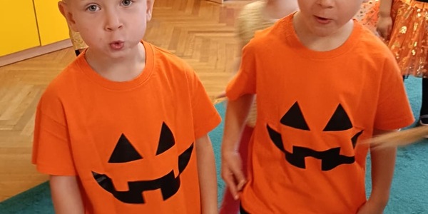 Dwóch chłopców bliźniaków stoją do zdjęciach w takich samych pomarańczowych koszulkach z uśmiechem.
