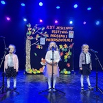 Trzy dziewczynki śpiewają do mikrofonów na scenie podczas konkursu piosenki.