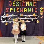 Dwie dziewczynki stoją na scenie i trzymają dyplomy.