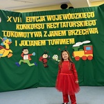 Dziewczynka pozuje do zdjęcia stojąc przed ścianką dekoracyjną.