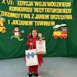 Dziewczynka pozuje do zdjęcia trzymając dyplom i nagrodę.