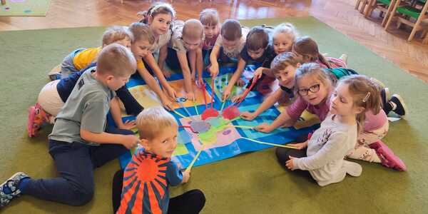 Dzieci siedzą wokół maty z liczbami i dotykają za pomocą łapek odpowiedniego pola.
