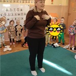 Nauczycielka w opasce misia inscenizuje piosenkę podczas Dnia Pluszowego Misia.