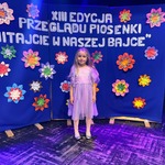 Dziewczynka pozuje do zdjęcia na ściance dekoracyjnej.