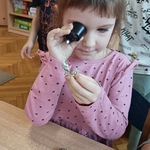 Dziewczynka ogląda eksponat za pomocą lupy.