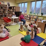 Dzieci siedzą na materacach i słuchają pani bibliotekarki czytającej opowiadanie.