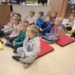 Dzieci siedzą na materacach i słuchają pani bibliotekarki czytającej opowiadanie.