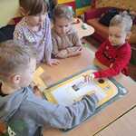 Dzieci układają planszę edukacyjną z odpadami.