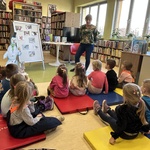 Dzieci słuchają pani bibliotekarki podczas zajęć edukacyjnych w bibliotece.