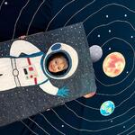 Chłopiec w fotościance astronauty pozuje do zdjęcia na tle maty Układu Słonecznego.