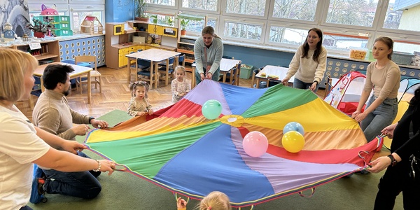 Dzieci wraz z rodzicami i nauczycielkami uczestniczą w zabawach z chustą animacyjną.