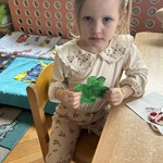 Dziewczynka trzyma zieloną koniczynkę wyciętą z papieru.