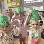 Trzy dziewczynki trzymają nad głową papierowe kapelusze Leprechauna.