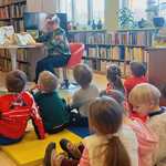 Dzieci słuchają opowiadania czytanego przez bibliotekarkę.