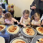 Dzieci nakładają sos pomidorowy na pizze.