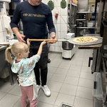 Dziewczynka z pomocą instruktora wkłada pizzę do pieca.