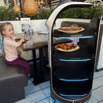 Robot przywozi pizzę do stolika dzieci.