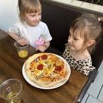 Dwie dziewczynki siedzą przy stoliku ze swoją pizzą.