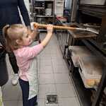 Dziewczynka wkłada pizzę do pieca.