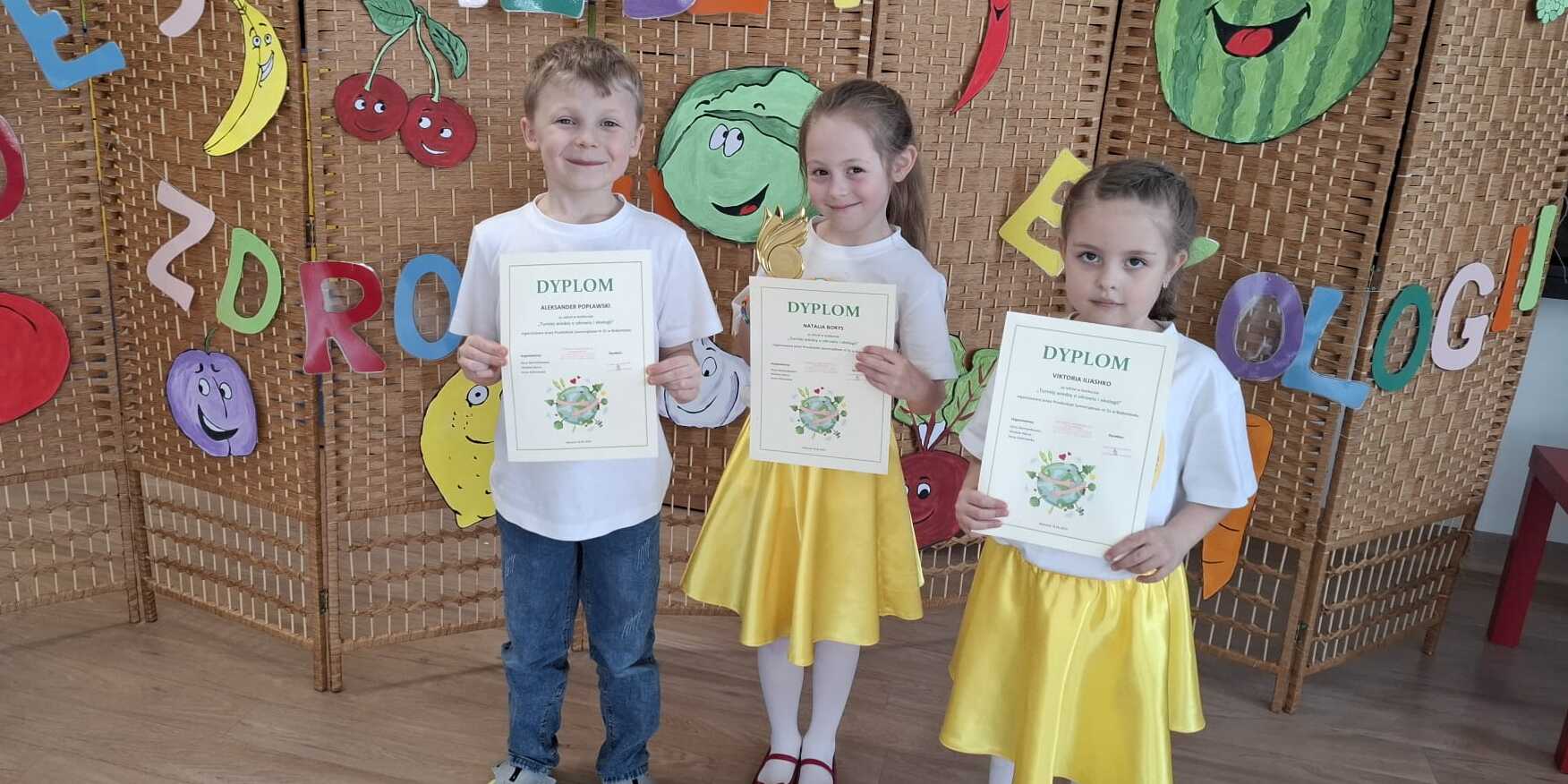 Trójka dzieci pozuje do zdjęcia z dyplomami i pucharem.
