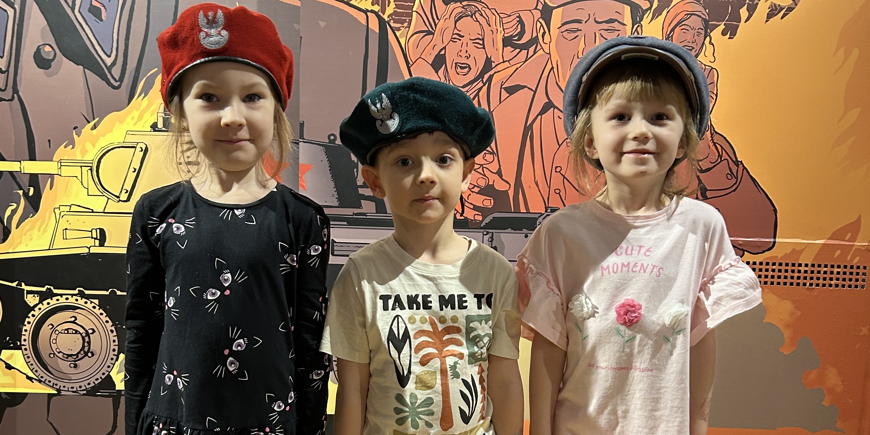 Troje dzieci pozuje do zdjęcia w wojskowych czapkach.