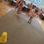 Dzieci biorą udział w zawodach sportowych. Dziewczynki przekładają obręcze przez swoje ciało. 
