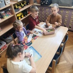 Dzieci siedzą przy stole i kolorują kredki z papieru.