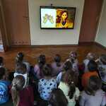Dzieci siedzą na dywanie i oglądają film edukacyjny.