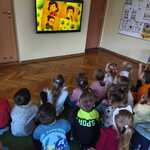 Dzieci siedzą na dywanie i oglądają film edukacyjny.