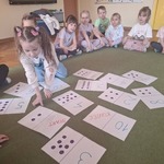 Dziewczynka przelicza liczbę kropek na przygotowanych kartkach. Dopasowuje po kolei zgromadzone wyniki od najmniejszej do największej. 