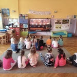 Dzieci siedzą na dywanie i oglądają na monitorze film edukacyjny o teatrze. Na ekranie widać widownię.