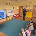 Dzieci siedzą na dywanie i słuchają co mówi instruktor.