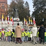 Dzieci wraz z nauczycielami stoją pod pomnikiem Świętego Jana Pawła II.