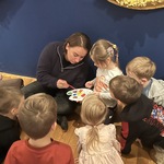 Dziewczynka z pomocą pani przewodnik tworzy barwy pochodne na palecie, inne dzieci się przyglądają.